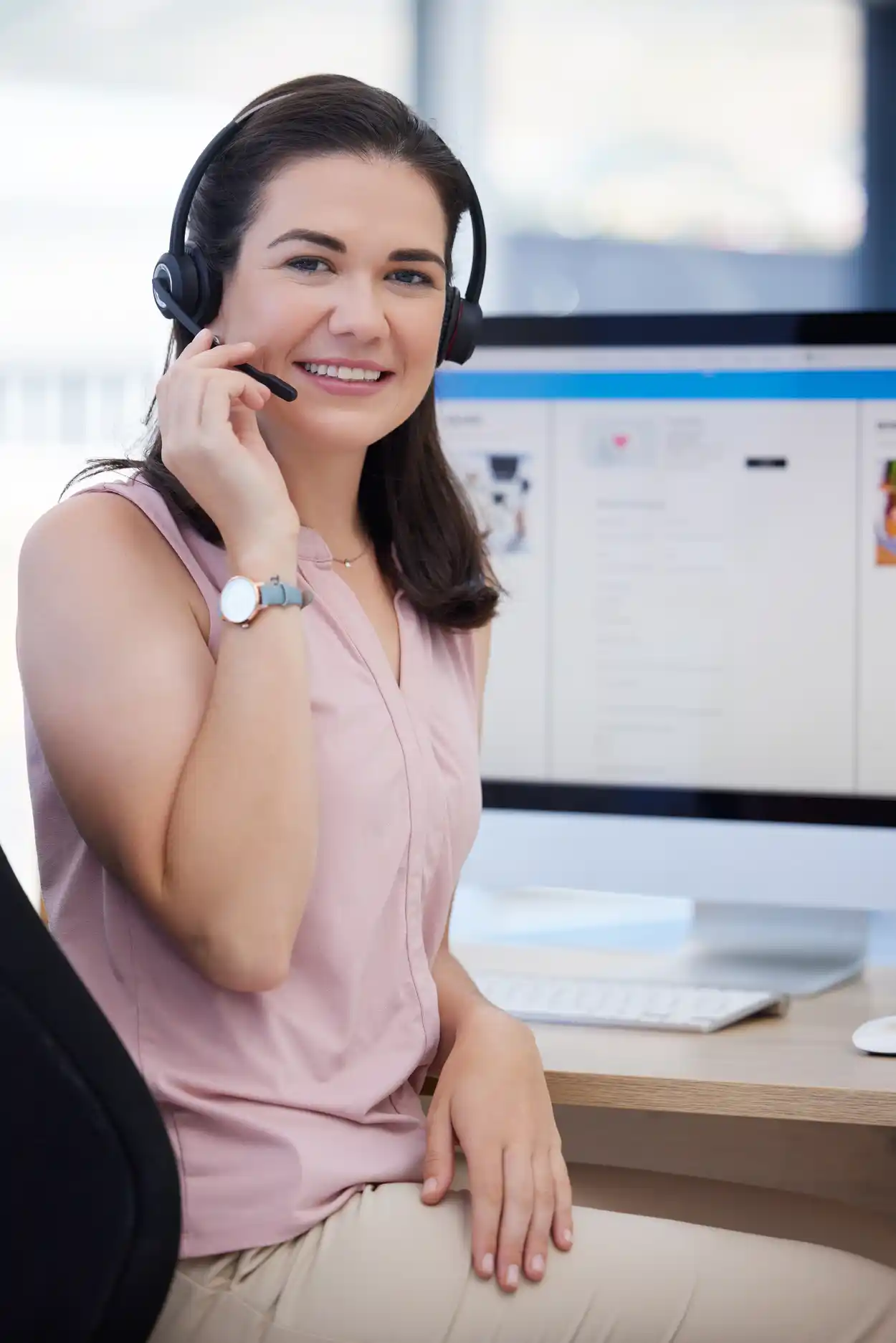 Customer service representative with a headset smiling in front of a computer screen displaying an e-commerce platform website.